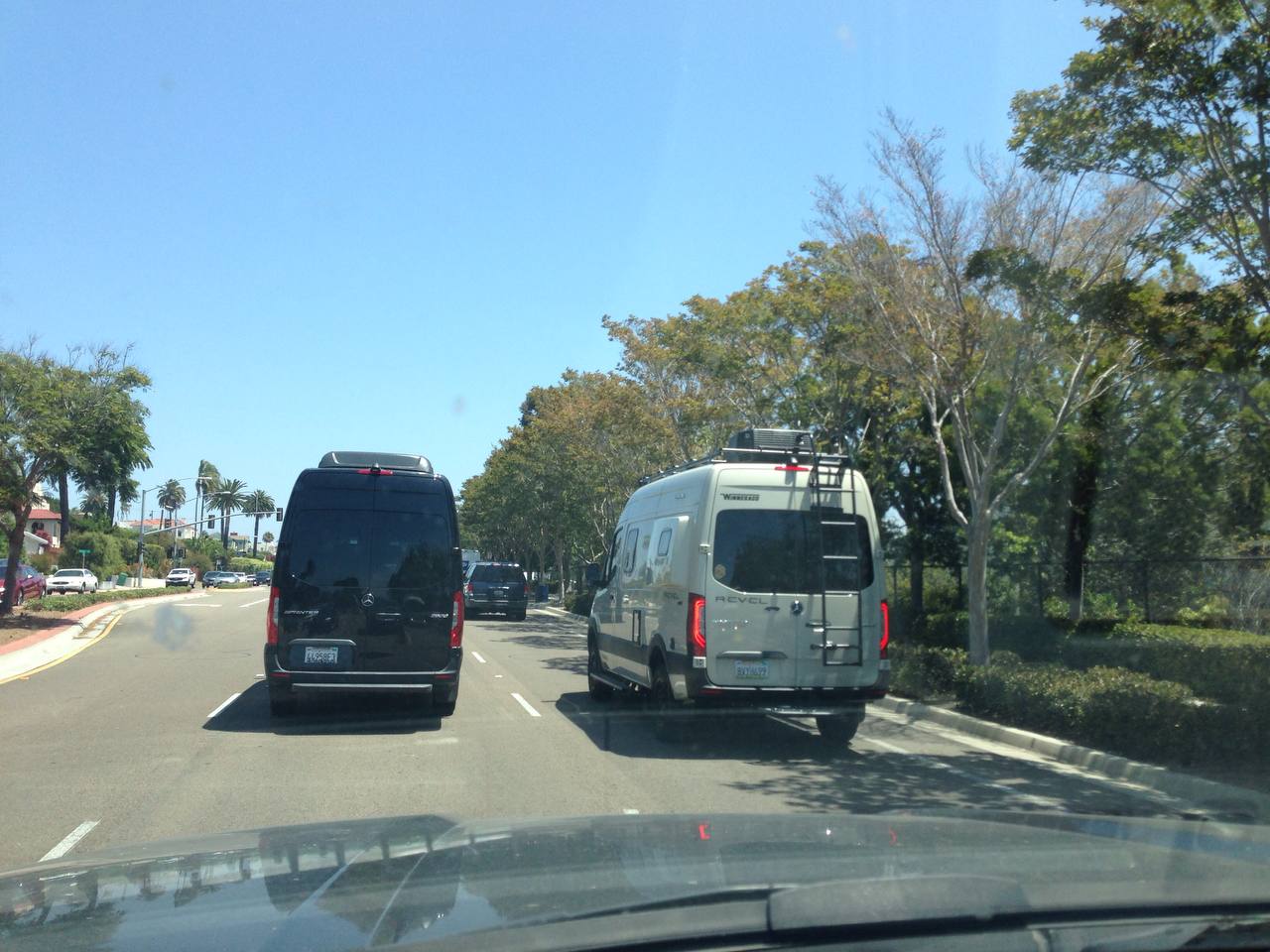 Black Sprinter van and camper van driving on a tree-lined road — Sprinter Rentals Chicago van rental
