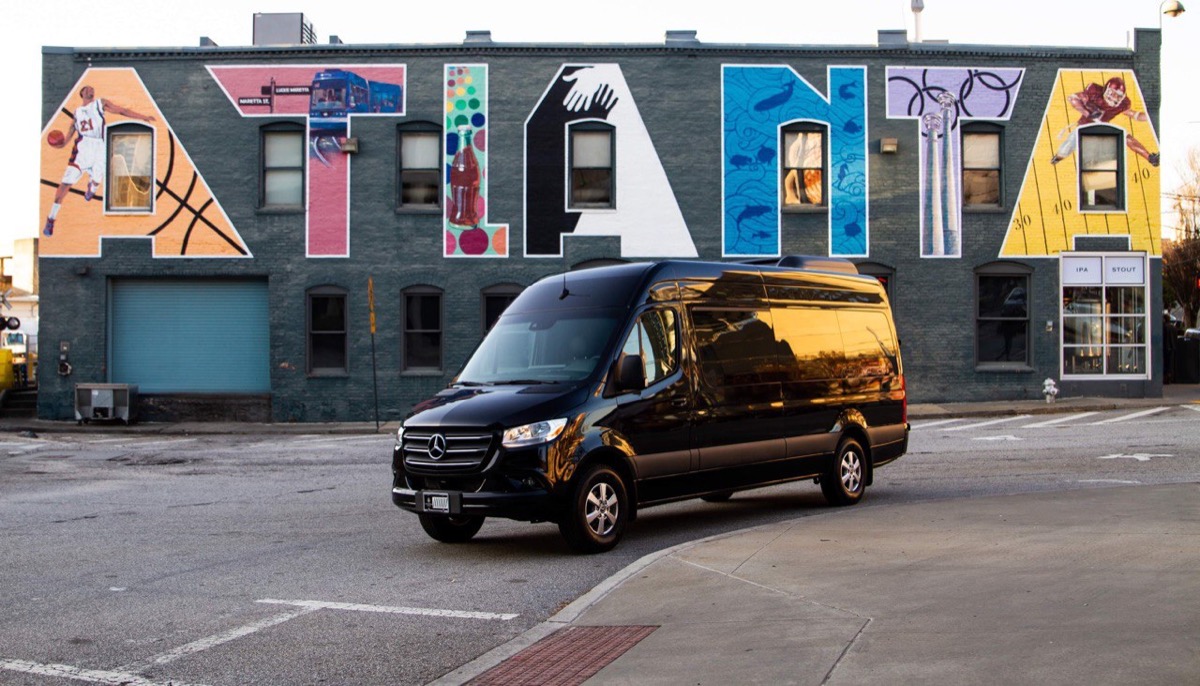 Black Mercedes-Benz Sprinter van rental parked in front of colorful Atlanta mural featuring iconic city landmarks and culture