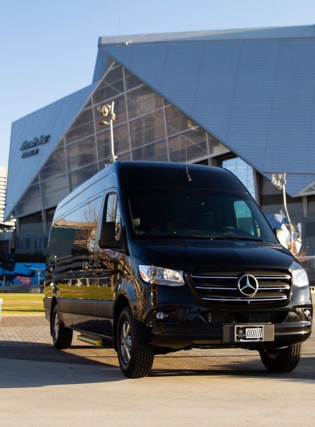 Front view of black Mercedes-Benz Sprinter van rental with Mercedes-Benz Stadium Atlanta in background on a clear day