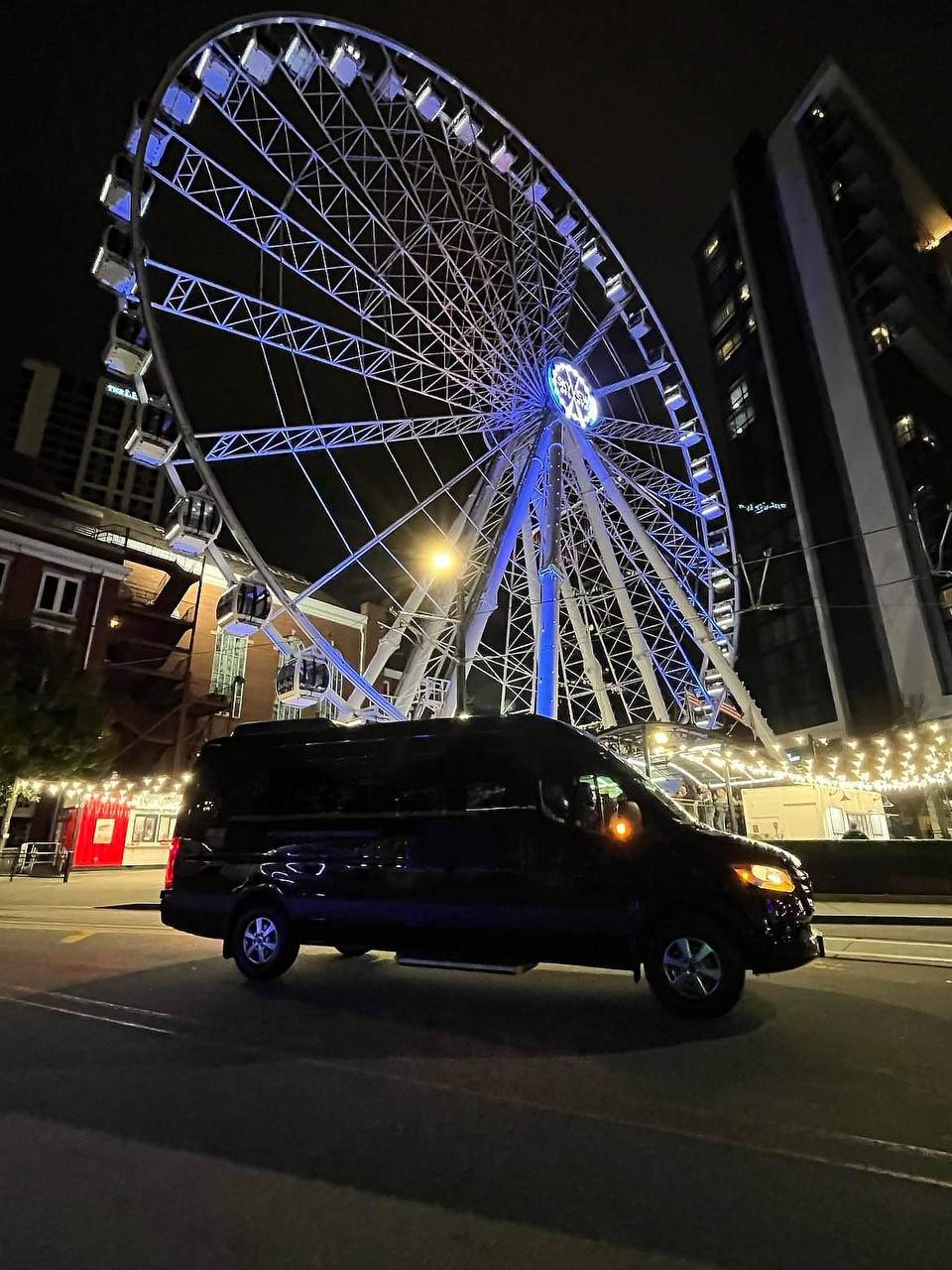 Sprinter van rental parked at SkyView Atlanta Ferris wheel at night with illuminated downtown Atlanta skyline